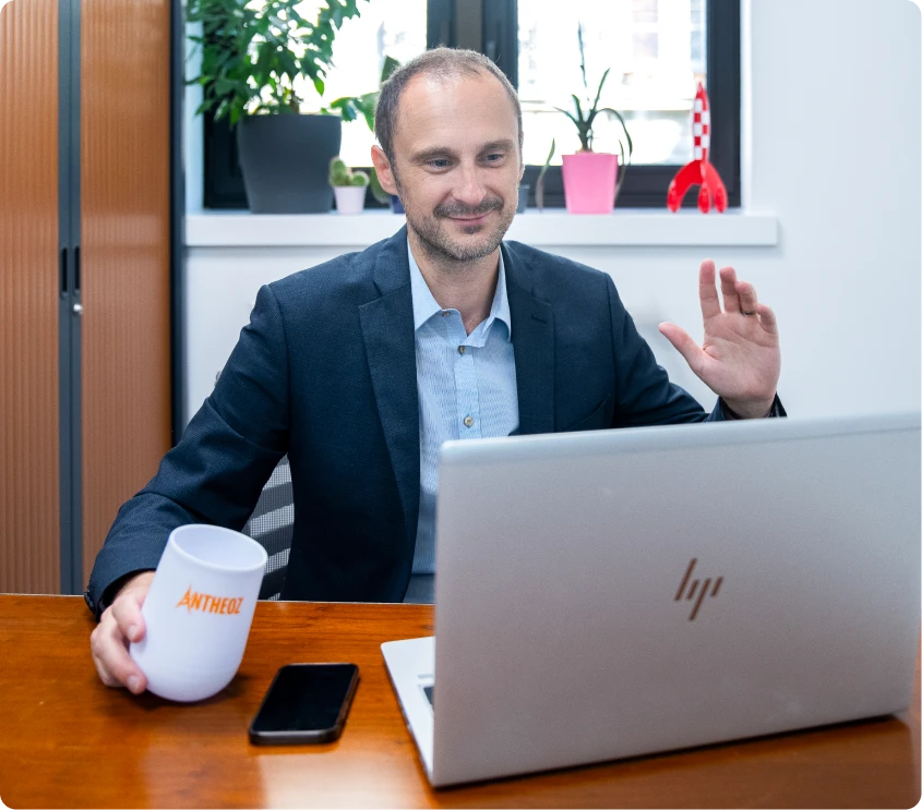 Un expert-comptable souriant en visioconférence avec un client, tenant un café, prêt à conseiller les entreprises depuis son cabinet à Paris.