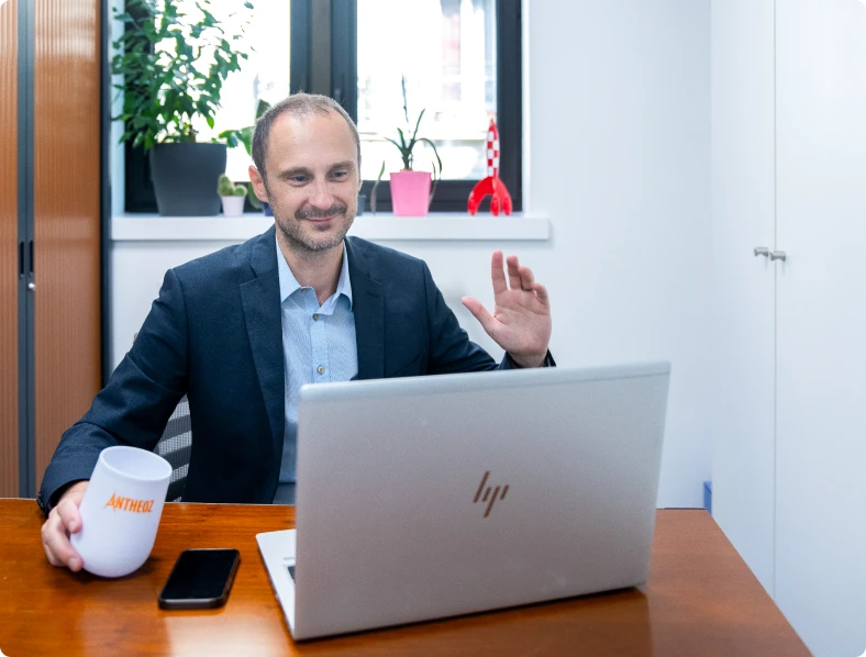 Un expert-comptable souriant en visioconférence avec un client, tenant un café, prêt à conseiller les entreprises depuis son cabinet à Paris.