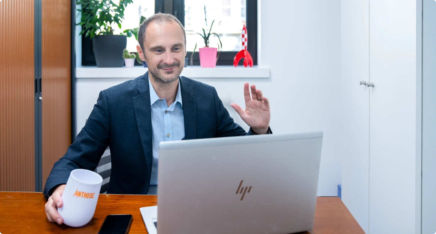 Un expert-comptable souriant en visioconférence avec un client, tenant un café, prêt à conseiller les entreprises depuis son cabinet à Paris.